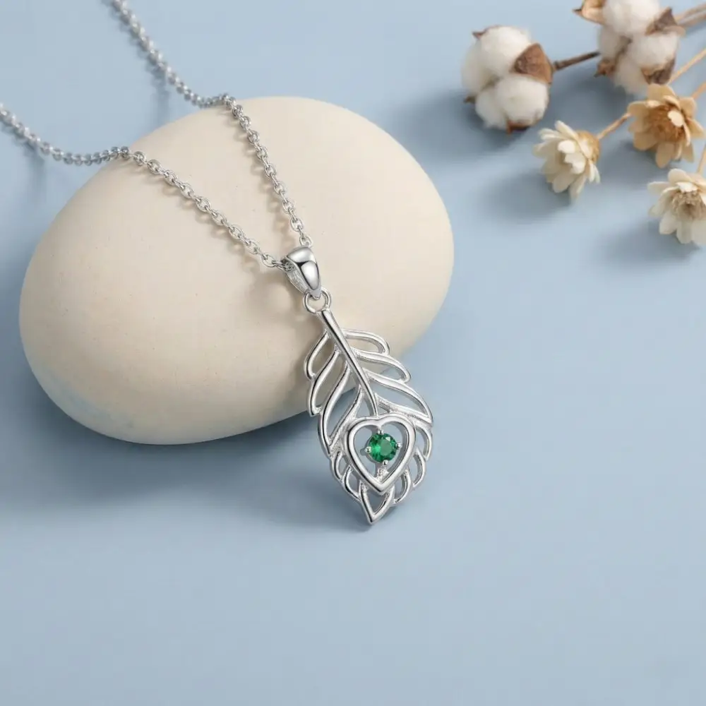 Elegant Green Stone Mor Pankh Necklace Elegant 925 Silver Mor Pankh Pendant resting gracefully on a smooth white stone, surrounded by delicate dried flowers to showcase its premium finish.