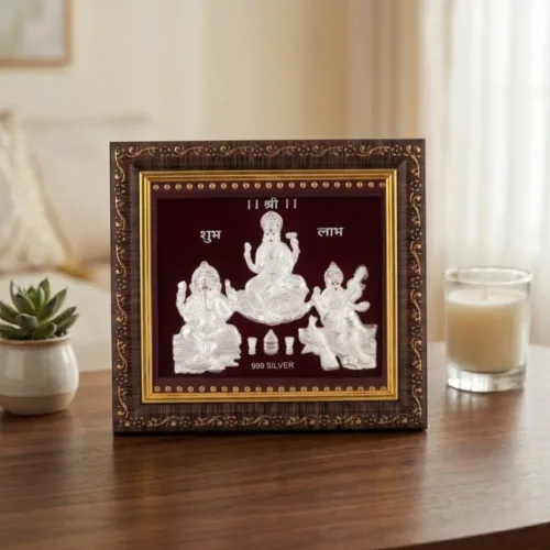 Beautiful pure silver laxmi ganesh saraswati frame for pooja room placed elegantly on a wooden table