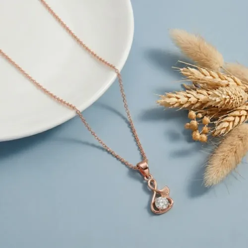 A beautifully styled minimalist rose gold jewellery piece resting on a white plate with dry wheat stalks