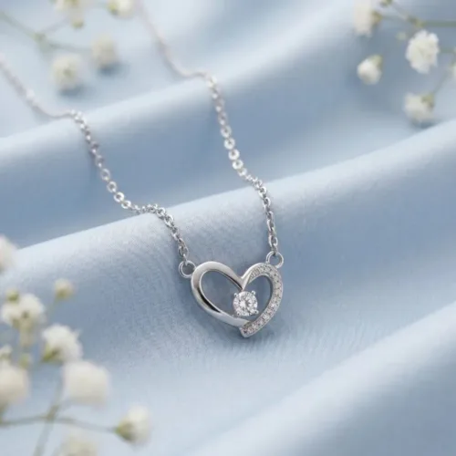 A beautifully styled romantic silver heart pendant necklace for gift resting delicately on soft blue silk fabric