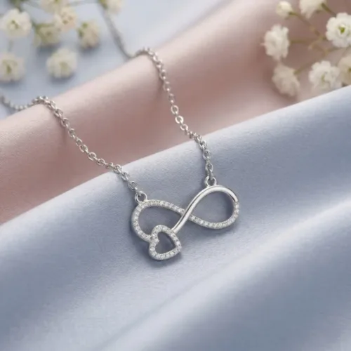 A beautifully styled romantic infinity heart pendant necklace resting elegantly on soft pastel silk fabric