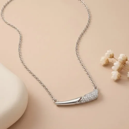 A beautifully styled simple silver necklace for daily wear resting elegantly beside delicate white flowers