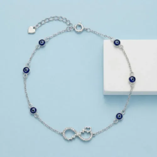 Top view of the sparkling evil eye silver anklet featuring a CZ studded infinity heart on a soft blue background