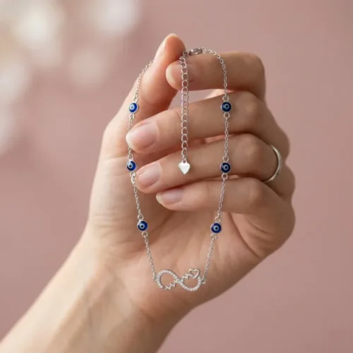 Woman delicately holding the modern evil eye payal silver showing its sparkling infinity pendant and blue protective beads