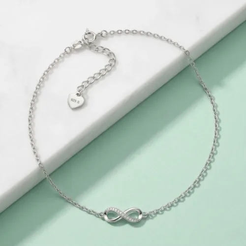 Top view of the minimal infinity silver anklet resting elegantly on a white marble and pastel green background