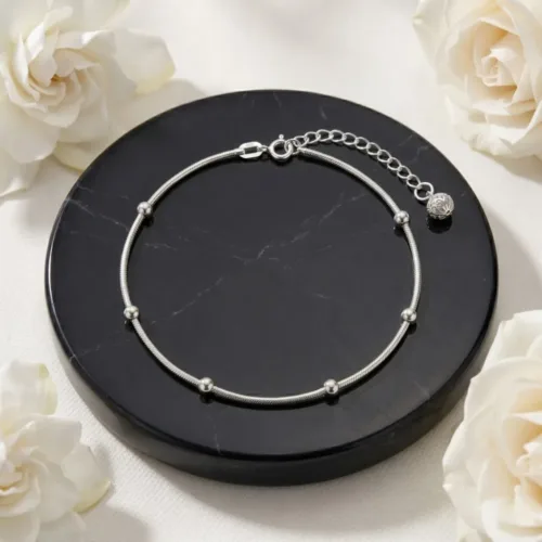 Beautiful top view of the silver beaded anklet for women resting on a premium black marble display with white flowers