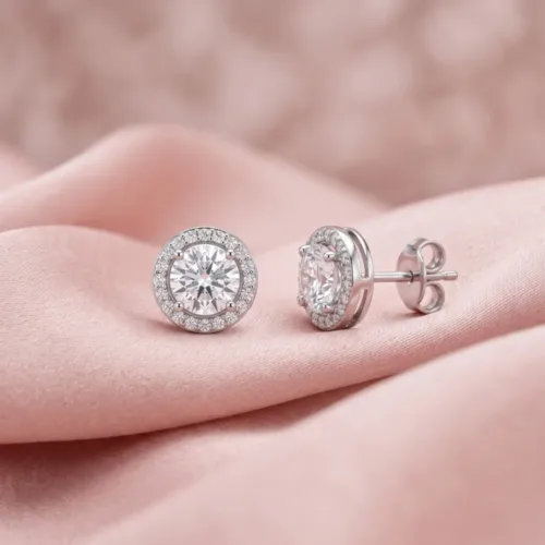 Beautiful silver halo stud earrings resting on a soft pink silk fabric, highlighting the brilliant American diamond center stone.