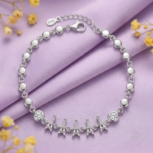 Close-up of the Eiffel Tower charm bracelet for women, highlighting the S925 authenticity stamp and two bezel-set CZ accent stones against a soft purple background.