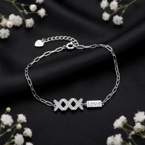 Elegant silver hugs and kisses bracelet displayed on a black background surrounded by delicate white flowers, highlighting the romantic love tag design.