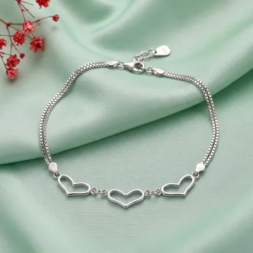 Elegant silver open heart link bracelet laid gracefully on a soft green silk fabric, highlighting its romantic design and shiny double box chain.