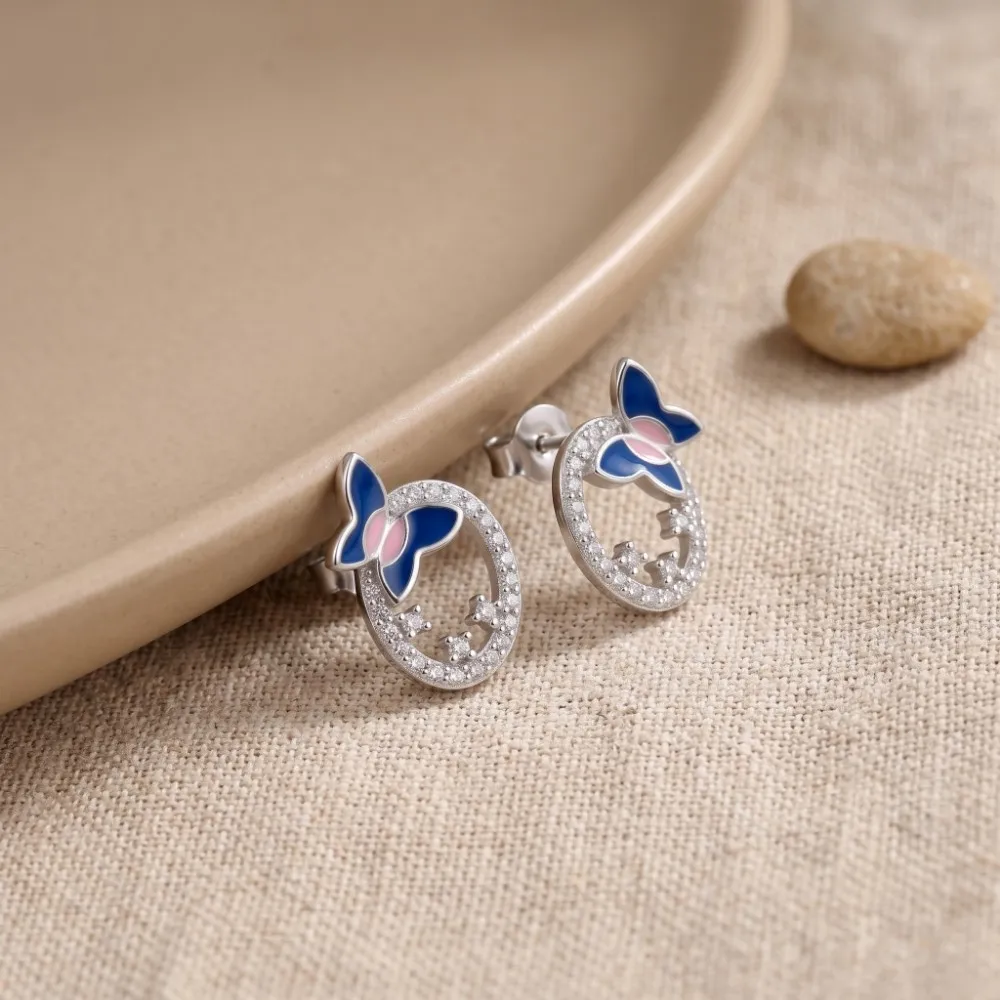 Silver Enamel Butterfly Earrings Angled close-up of the silver enamel butterfly earrings resting gracefully on a soft beige texture, highlighting the flawless finish of the oval frame.