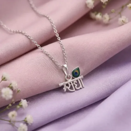 The radha name locket silver resting elegantly on pink silk, highlighting its detailed bansuri and enamel work.