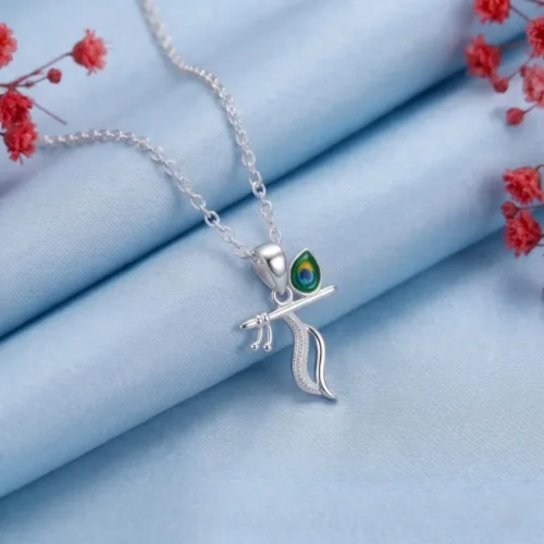 Krishna silver locket with enamel peacock feather and flute on light blue cloth beside red flowers