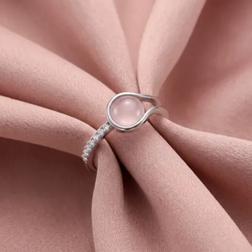 The beautiful silver wrap ring with pink stone resting elegantly on soft pink fabric, highlighting the soothing, natural glow of the center gem.