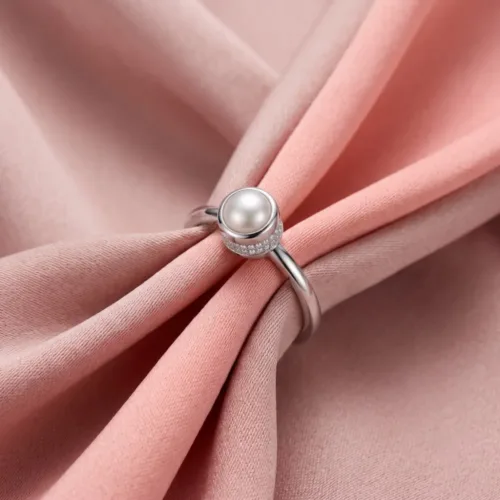 The beautiful pearl ring with american diamond resting elegantly on soft pink silk fabric, showcasing the classic hidden halo sparkle.
